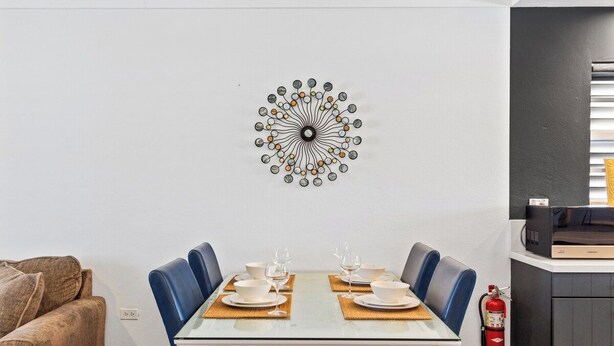 A dining area with a white table set for four, blue chairs, and a decorative wall piece.