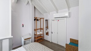 A bedroom with a bed, a wooden shelf unit, a white wardrobe, and an air conditioning unit.