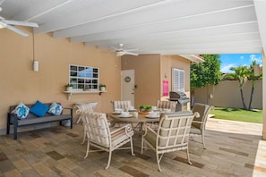 An outdoor patio with a round table, white wicker chairs, a ceiling fan, and a grill.