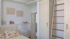 Un dormitori amb un llit, un armari, una escala i un escriptori amb una làmpada.