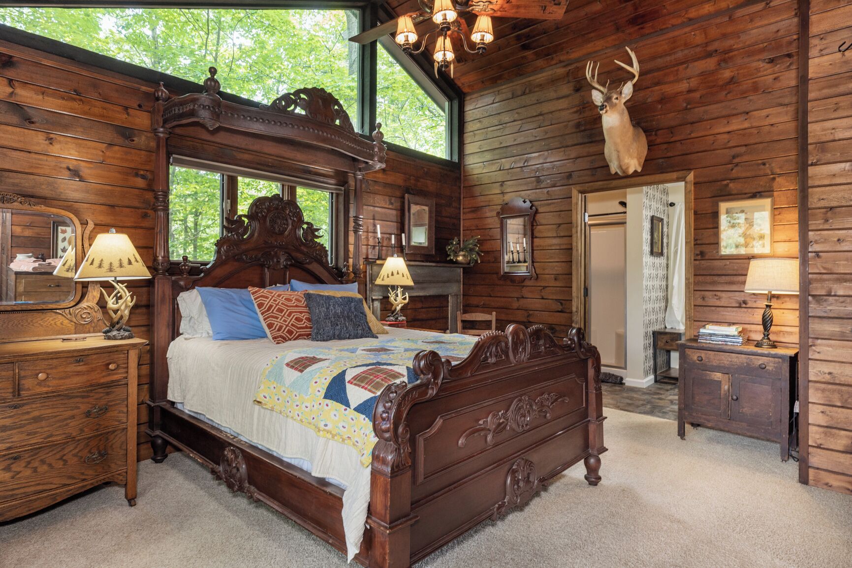 A log cabin bedroom with a large bed, wooden headboard, and a deer head mounted on the wall.