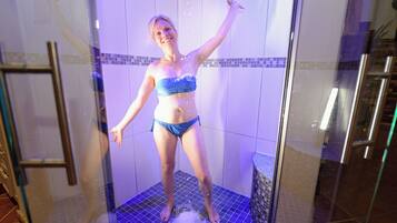A person in a shower with a tiled floor and a glass door.