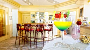 A bar area with a bar counter, multiple chairs, and a table with a colorful drink and a bowl of nuts. - Wellnesshotel Rothfuss mit Spa und 2 Schwimmbädern (Bad Wildbad)