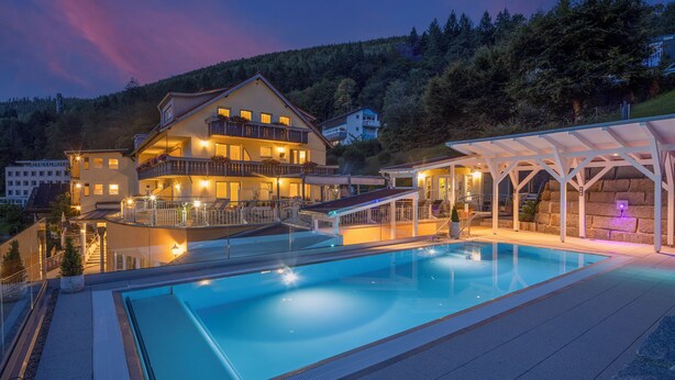 A hotel with a swimming pool, a covered outdoor area, and a mountain backdrop. - Wellnesshotel Rothfuss mit Spa und 2 Schwimmbädern (Bad Wildbad)