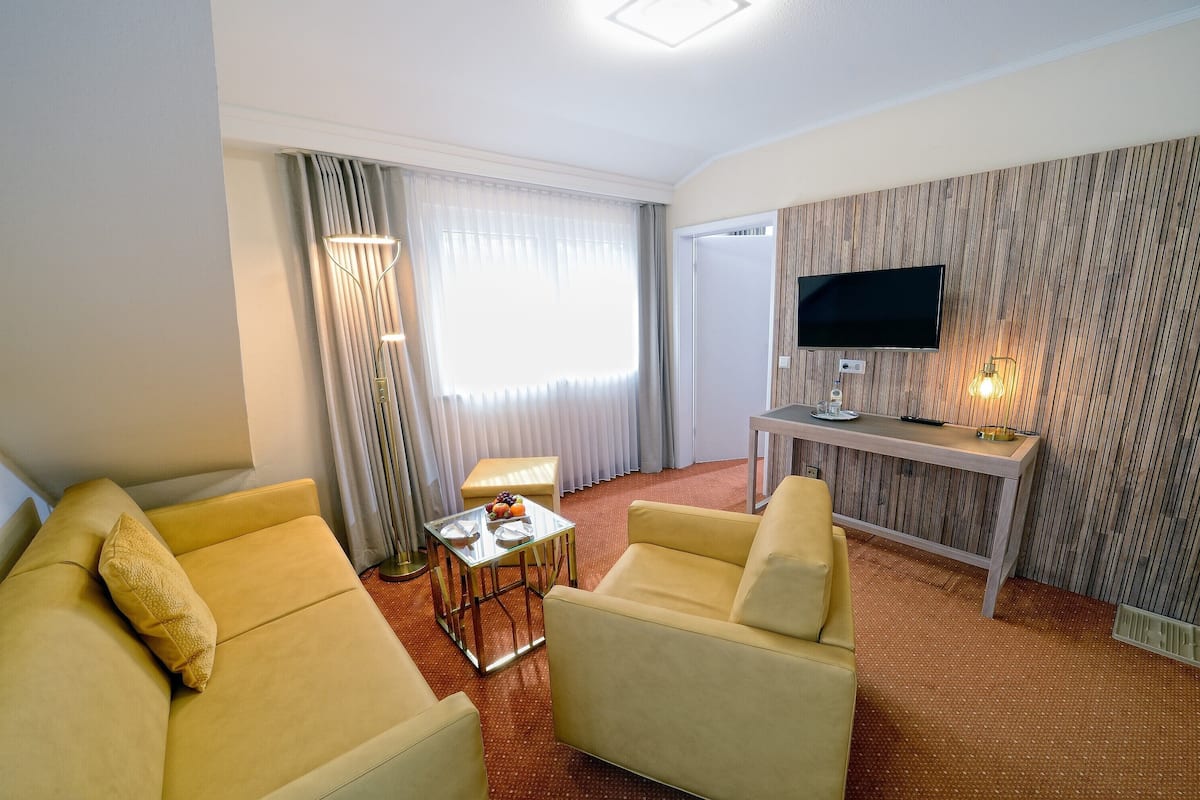 A hotel room with a sofa, a small table with fruit, a TV, and a wooden wall panel.