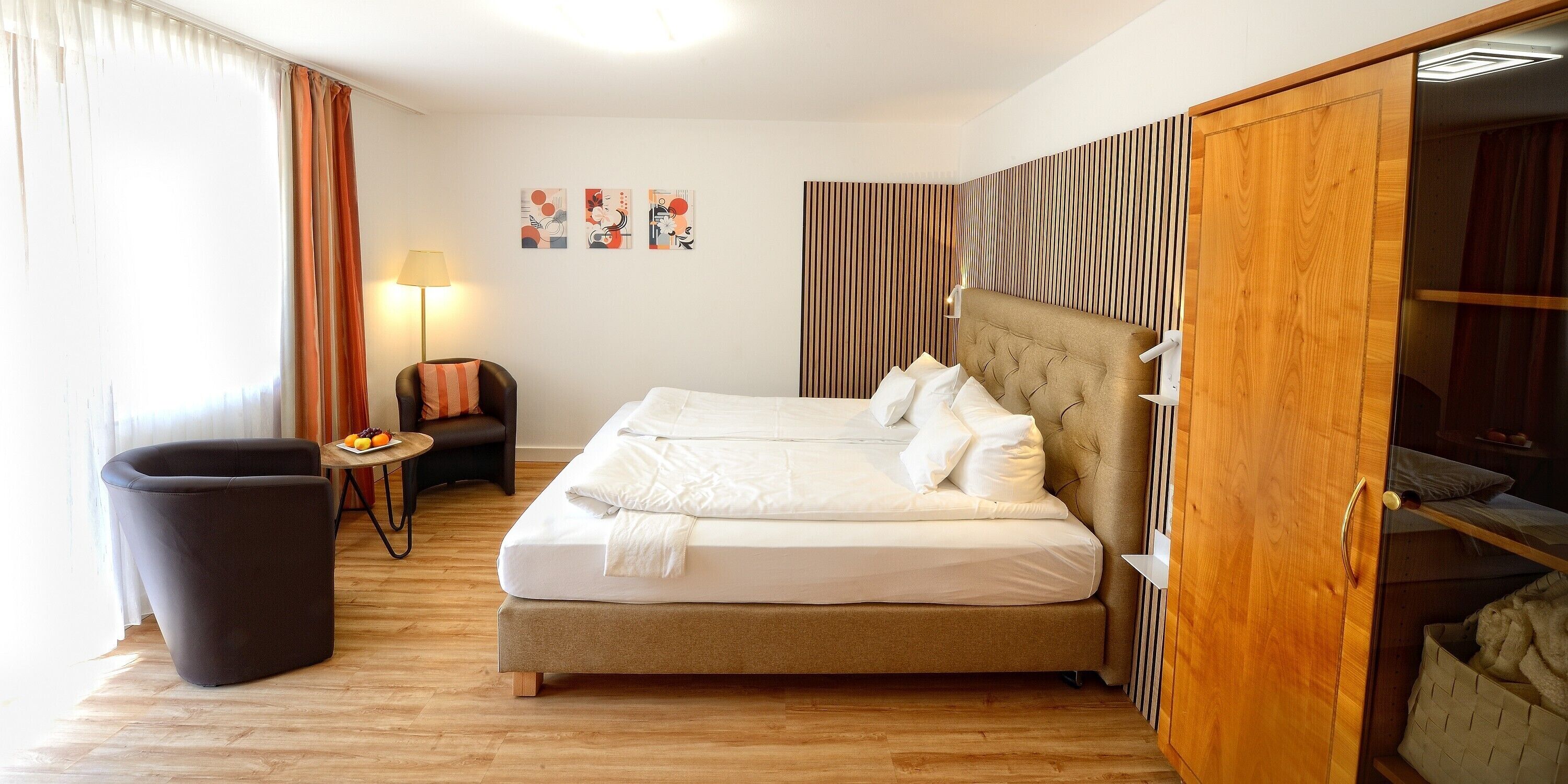 A hotel room with a bed, a chair, a lamp, and artwork on the wall.