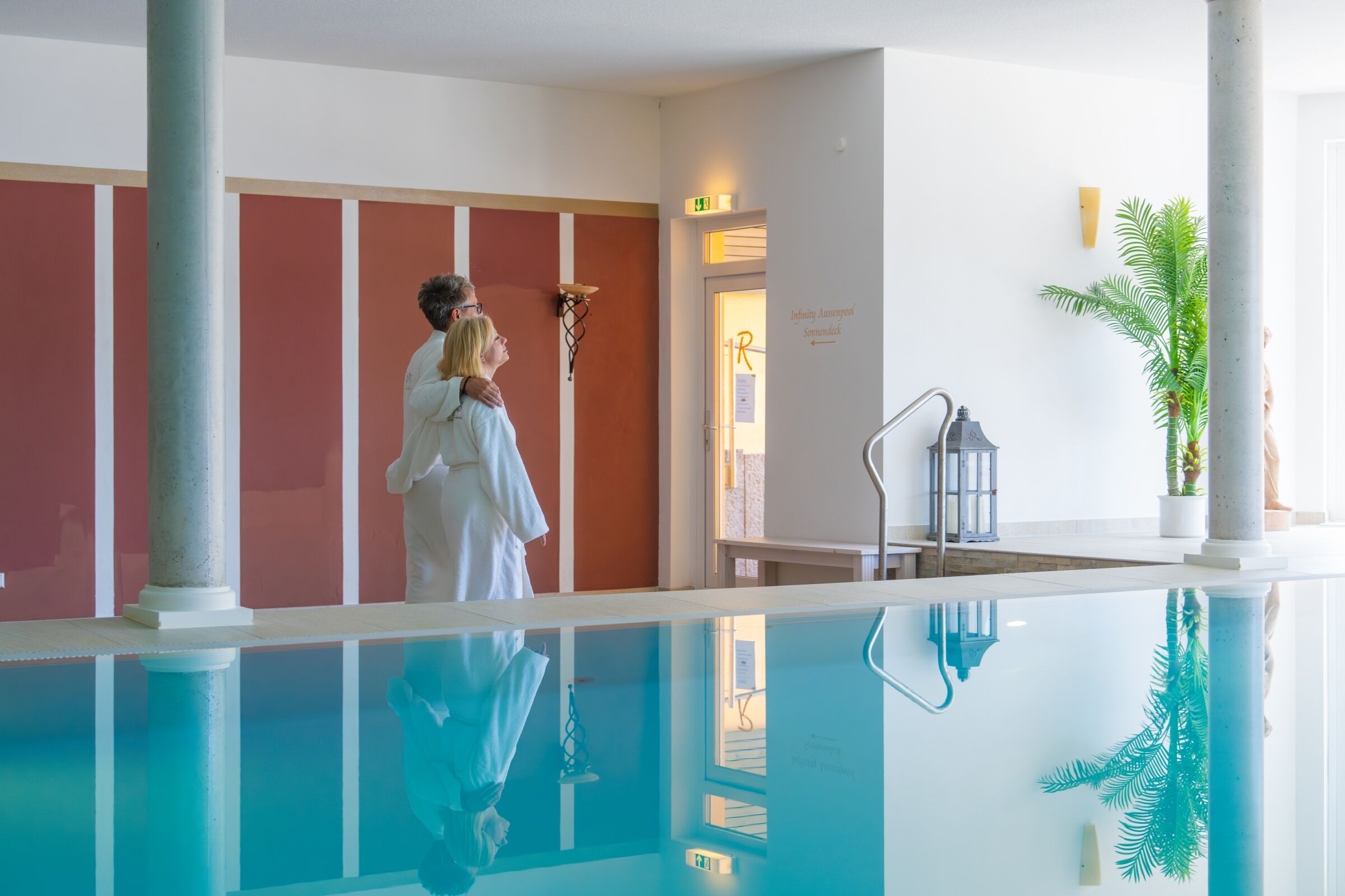 A swimming pool with a clear reflection, a couple embracing, and a plant in the corner.