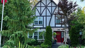 Une maison à deux étages avec une porte rouge, entourée d’un jardin bien entretenu et d’arbres.