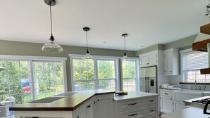 Une cuisine moderne avec des meubles blancs, un îlot central en bois et des luminaires suspendus.