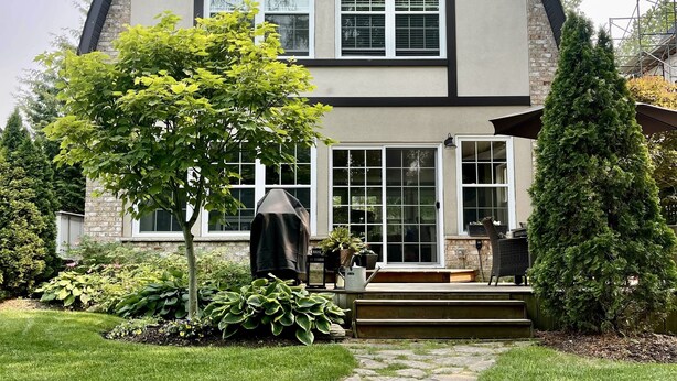 Une maison à deux étages, avec des fondations en pierre, une grande véranda à l’avant et un espace barbecue couvert.