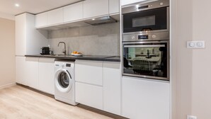 A modern kitchen with a built-in washing machine, a double oven, and a stainless steel range hood. - Sweett | Madeleine I (Paris)