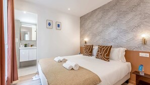 A hotel room with a large bed, a bathroom visible through an open door, and a patterned wall. - Sweett | Madeleine I (Paris)