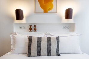 Un lit bien fait, avec des oreillers blancs et rayés, une tête de lit en bois et un luminaire fixé au mur, juste au-dessus.