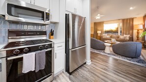 A modern kitchen with stainless steel appliances, a dining area with a gray sofa, and a view of the living room. - Sunlit La Jolla Village Gem with Peak Ocean Views! (San Diego)