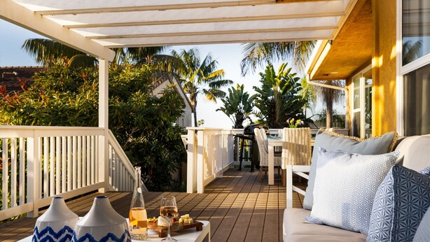A covered outdoor seating area with a white sofa, patterned cushions, and a table with decorative vases and a glass of wine. - Sunlit La Jolla Village Gem with Peak Ocean Views! (San Diego)