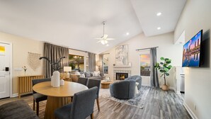 A modern living room with a dining area, a fireplace, and a TV mounted on the wall. - Sunlit La Jolla Village Gem with Peak Ocean Views! (San Diego)