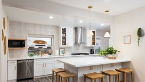 Una cocina moderna con armarios blancos, electrodomésticos de acero inoxidable y taburetes de bar de madera.