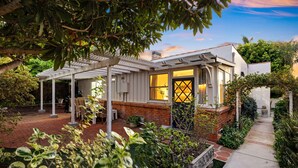 Una casa con porche cubierto, fachada de ladrillo y jardín con diversas plantas.