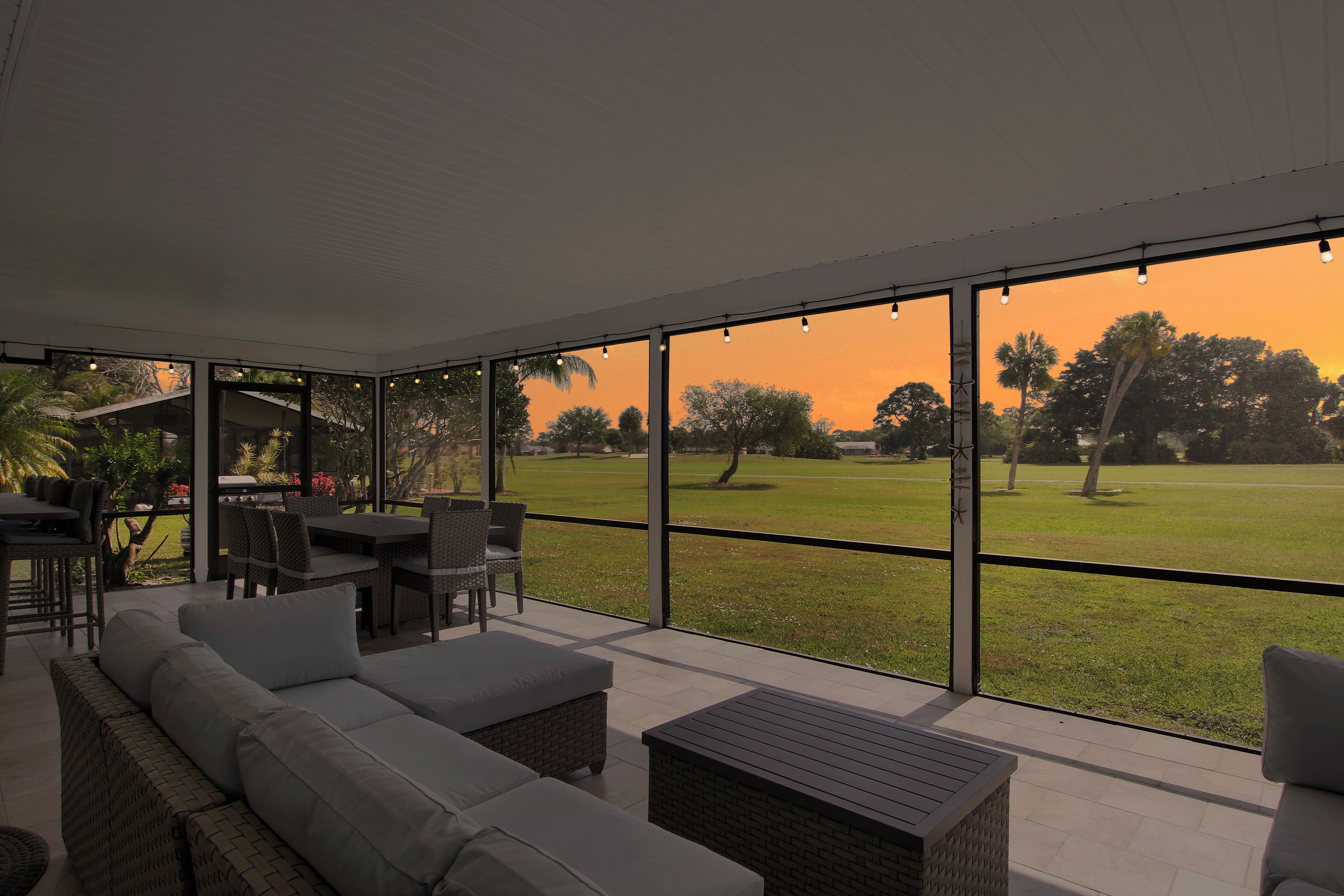 A spacious patio with a view of a grassy field and trees, furnished with a sofa, chairs, and a table.