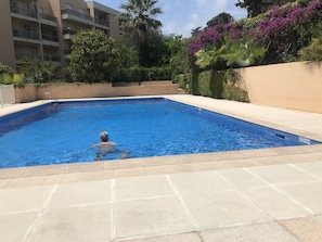 A swimming pool with a person in the water, surrounded by a building with balconies and lush greenery.