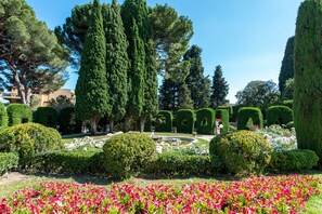 A well-manicured garden with neatly trimmed hedges, a variety of trees, and a central circular water feature.