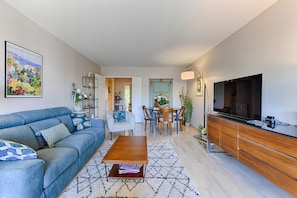 A modern living room with a sofa, coffee table, dining table, and TV.