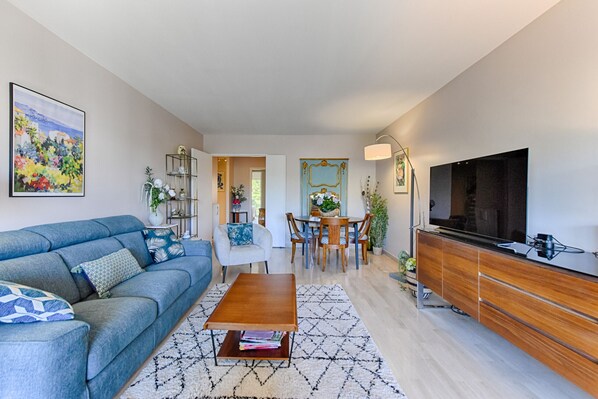 A modern living room with a sofa, coffee table, dining table, and TV.