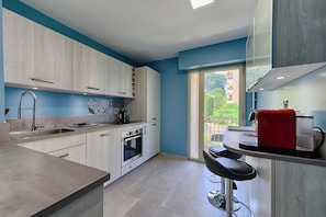 A modern kitchen with a built-in oven, a sink, and a bar area with a red appliance.