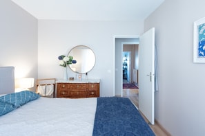 A bedroom with a bed, a dresser, a mirror, and a door leading to another room.