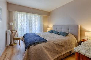 A bedroom with a large bed, a chair, a lamp, and a window with curtains.