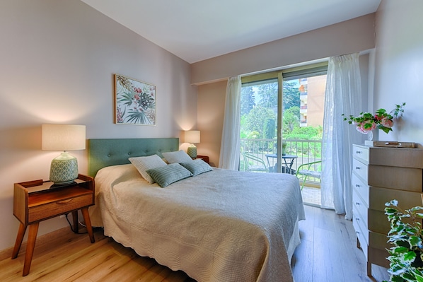 A bedroom with a bed, nightstands, a dresser, a window with curtains, and a balcony.