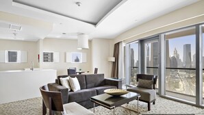 Una habitación de hotel moderna con un amplio ventanal que ofrece vista a la ciudad, un sofá, una silla, una mesita y un cuenco decorativo.