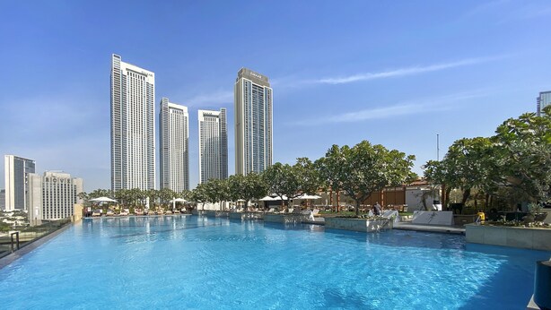 Una piscina con sillas de descanso y sombrillas, rodeada de edificios altos y árboles.