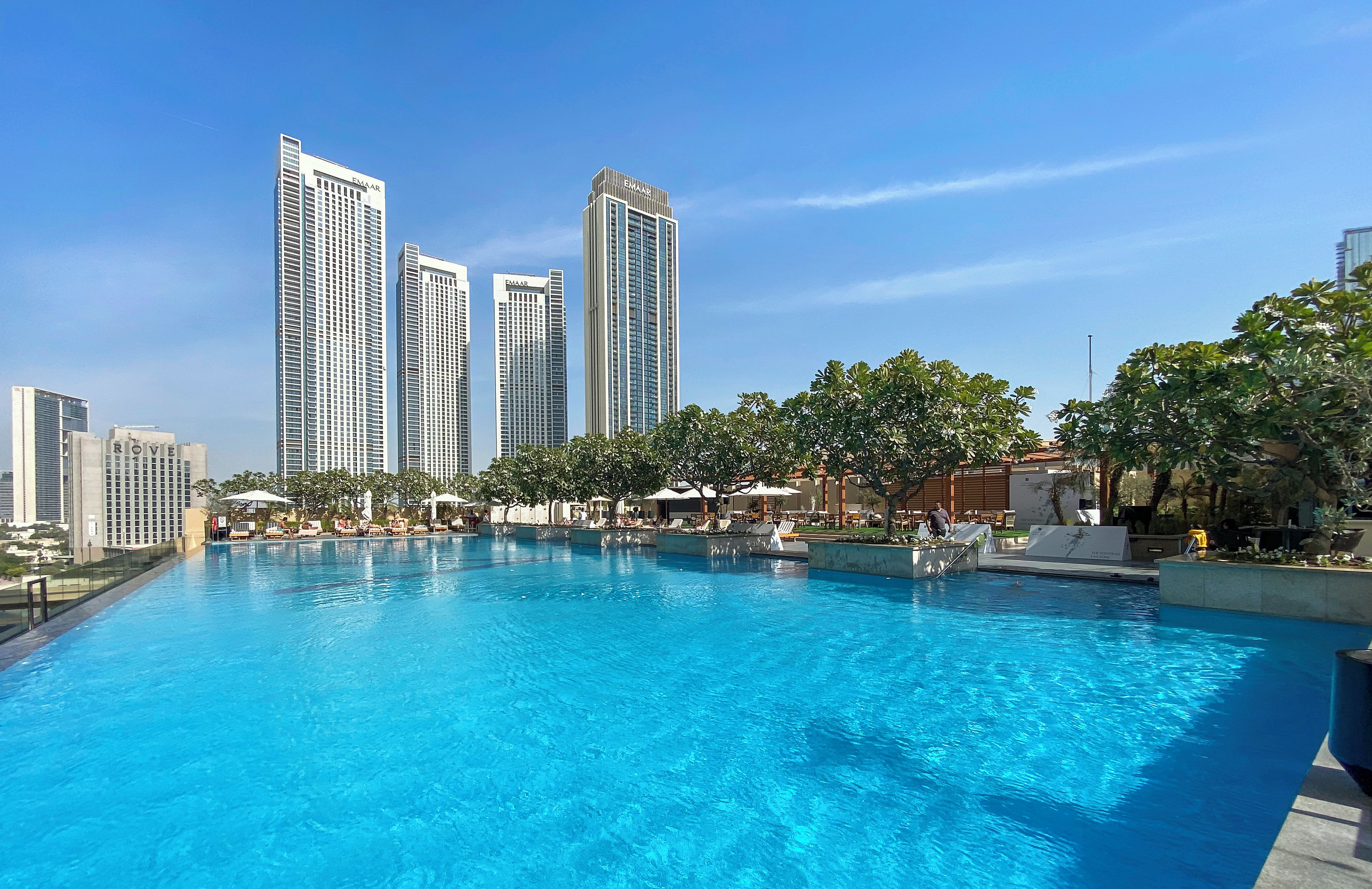 Una piscina con sillas de descanso y sombrillas, rodeada de edificios altos y árboles.