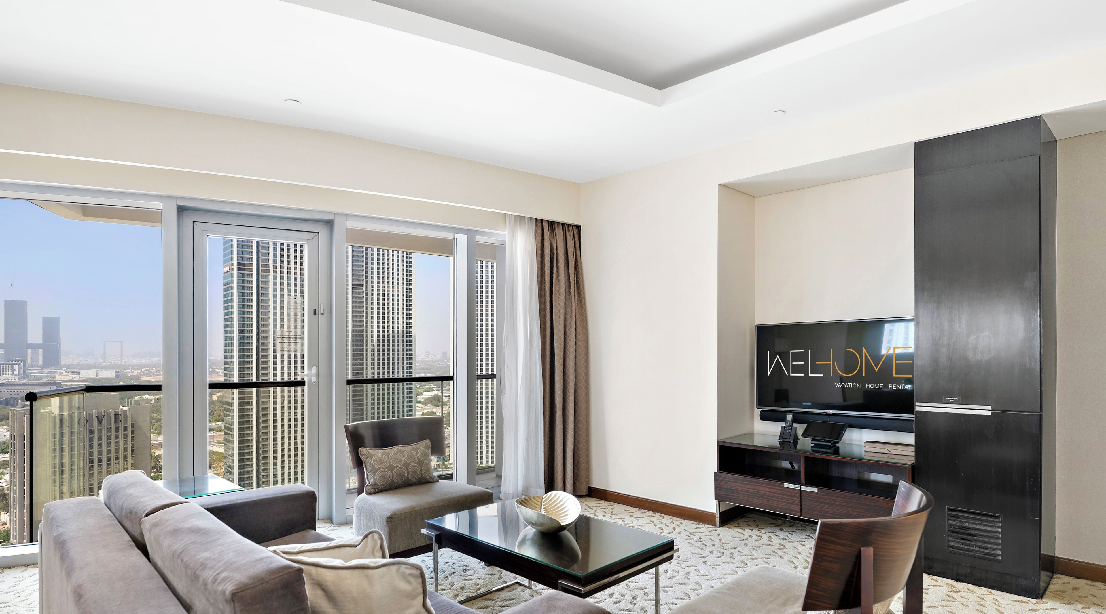 A modern living room with a sofa, armchair, and coffee table. A flat-screen TV is mounted on the wall.