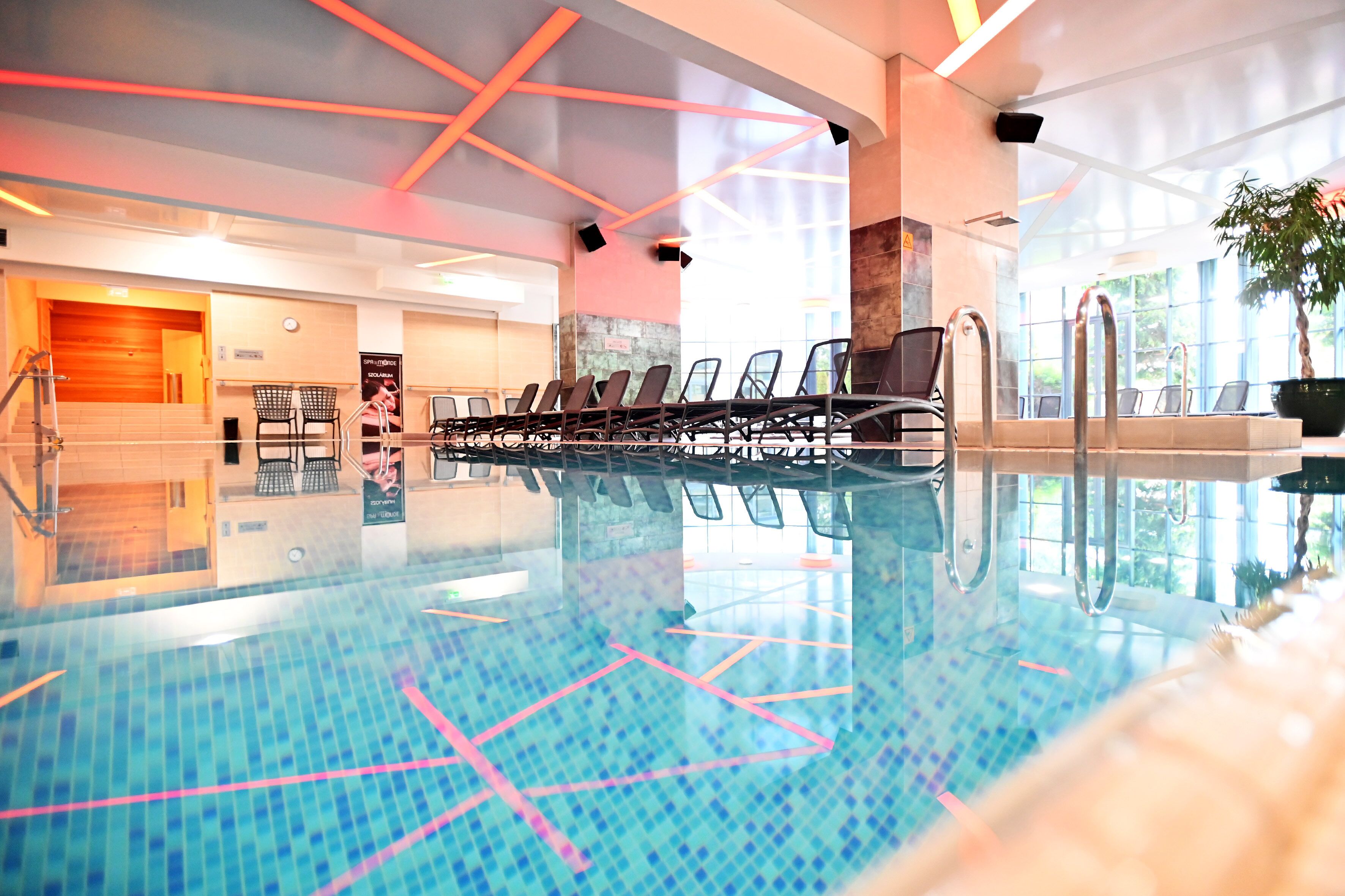 An indoor swimming pool with clear water, marked lanes, and a seating area with chairs.