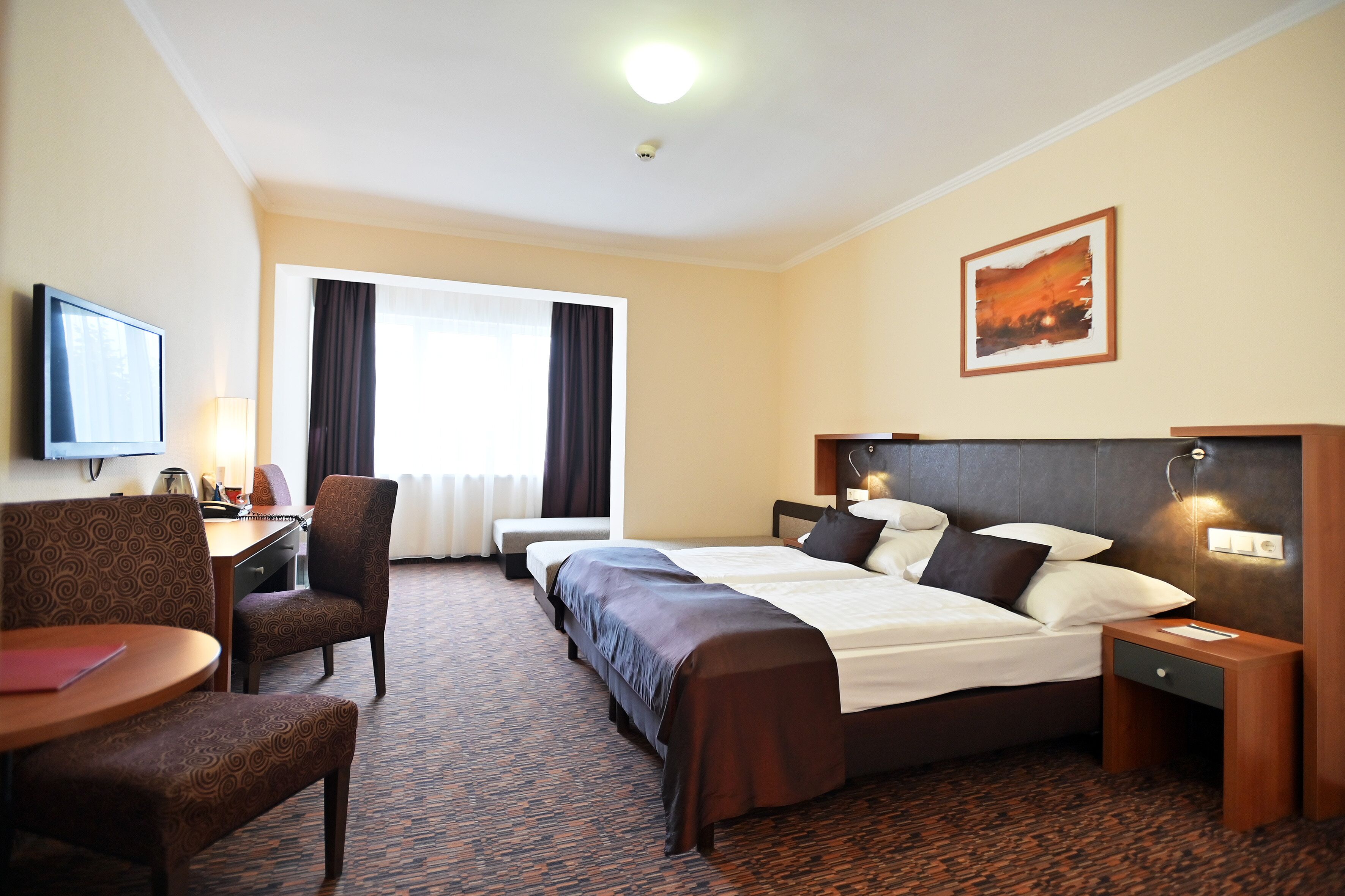 A hotel room with a large bed, a desk, a chair, a television, and a window with curtains.