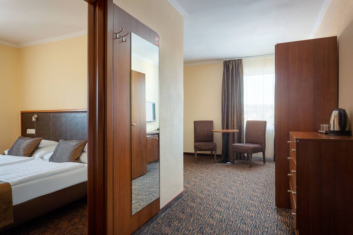 A hotel room with a bed, a desk, two chairs, a dresser, and a large mirror.