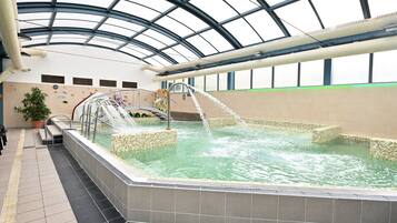 An indoor swimming pool with a glass ceiling, tiled walls, and a water fountain.