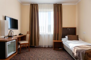 Habitación de hotel con una cama, un escritorio con televisor, una silla, una mesita y una ventana con cortinas.