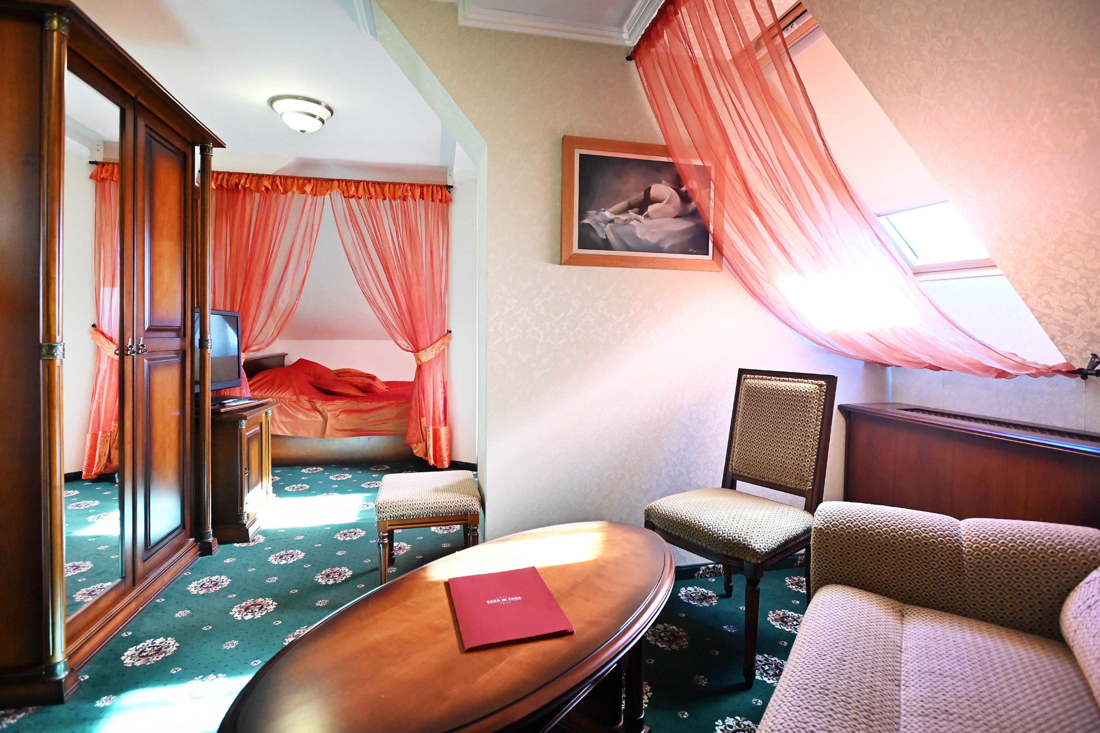 Ein Hotelzimmer mit einem Bett, einer Sitzecke inklusive Sessel, einem kleinen Tisch und einem großen Spiegel.