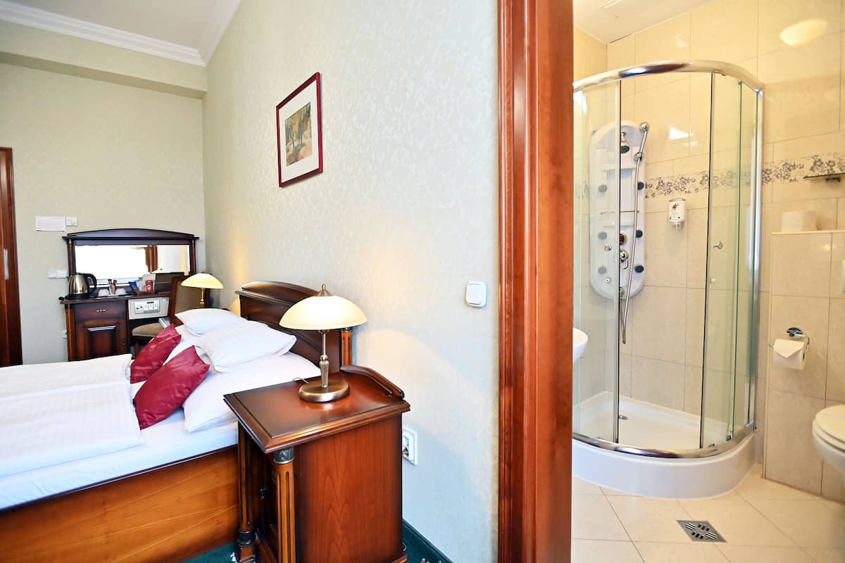 A hotel room with a bed, bedside table, lamp, and a glass-enclosed shower area.