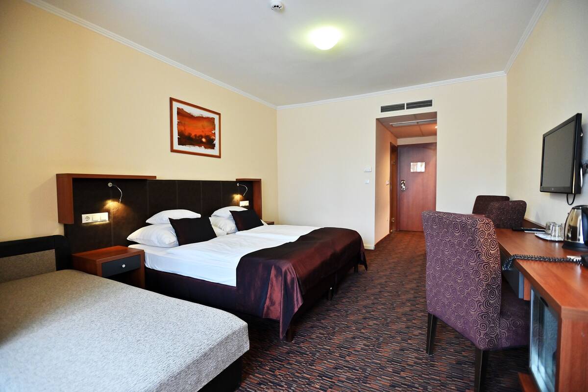 A hotel room with two beds, a desk with a chair, a television, and a painting on the wall.