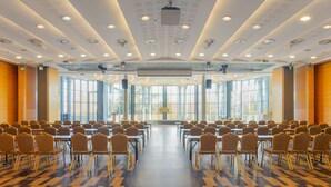 Una sala de conferències amb files de cadires i taules, finestres grans i un disseny de sostre modern.