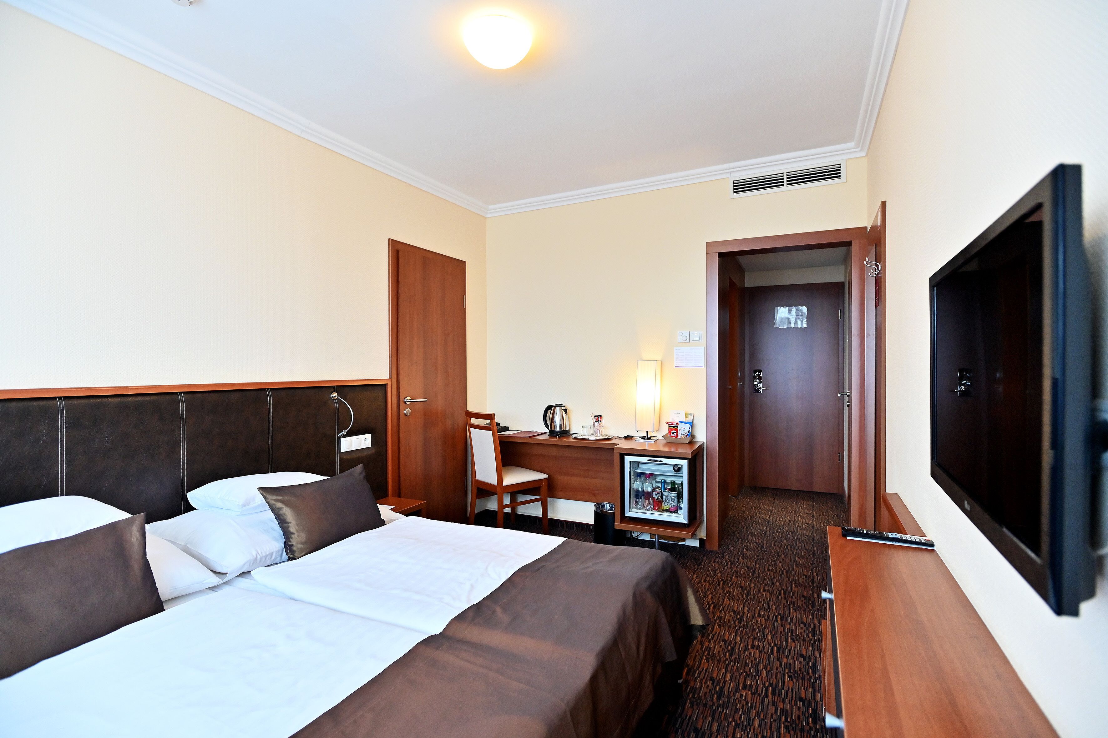 Habitación de hotel con una cama grande, un escritorio con silla, televisión y un minibar.