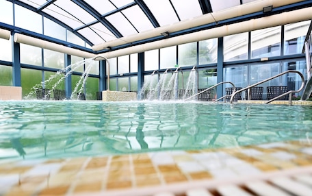An indoor swimming pool with clear water, surrounded by a glass enclosure and metal railings.