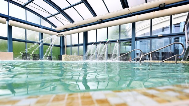 Una piscina interior amb aigua cristal·lina, envoltada d'un envà d'acer i baranes metàl·liques.