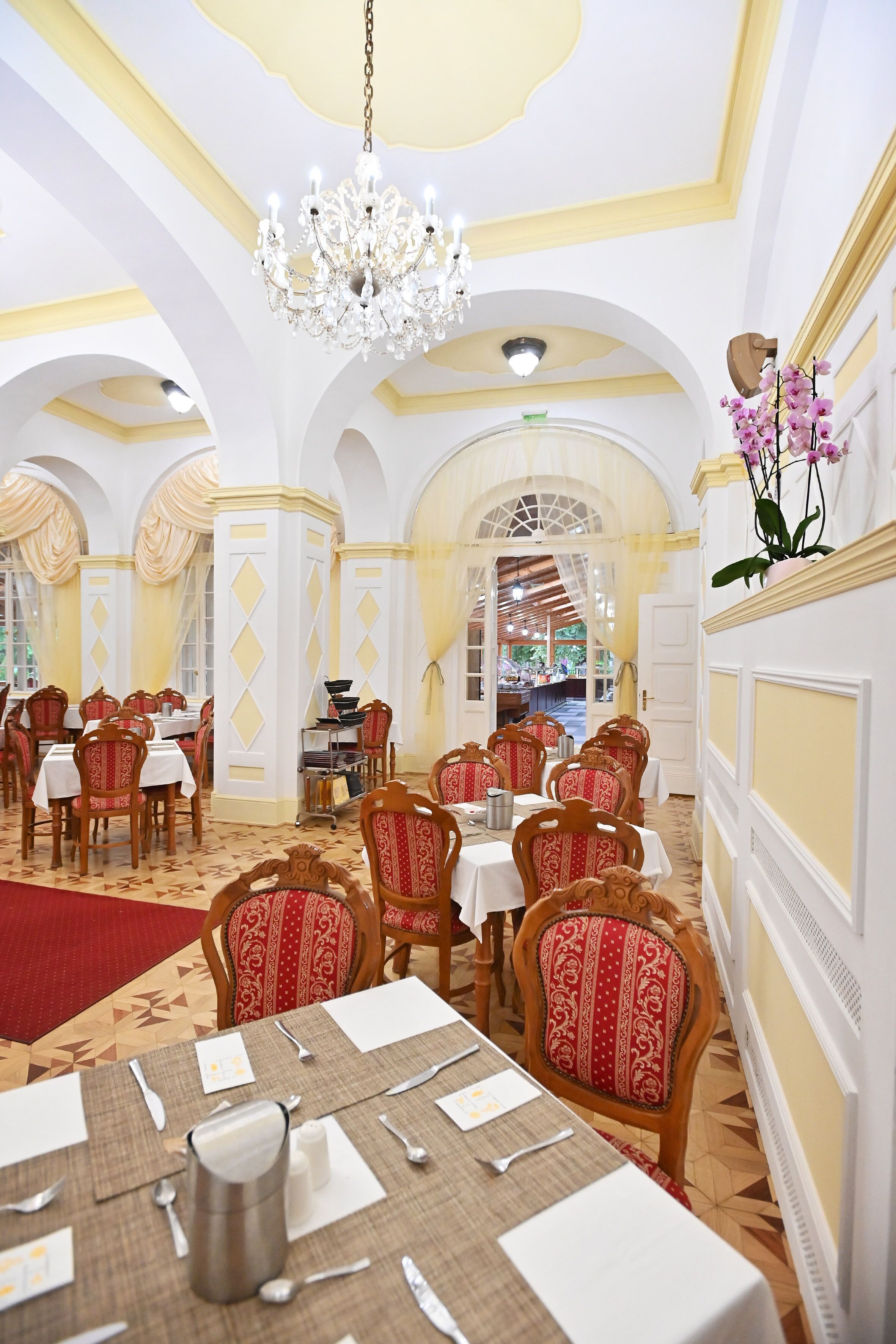 Une salle à manger avec des tables dressées pour le service, des lustres et des chaises décorées avec soin.