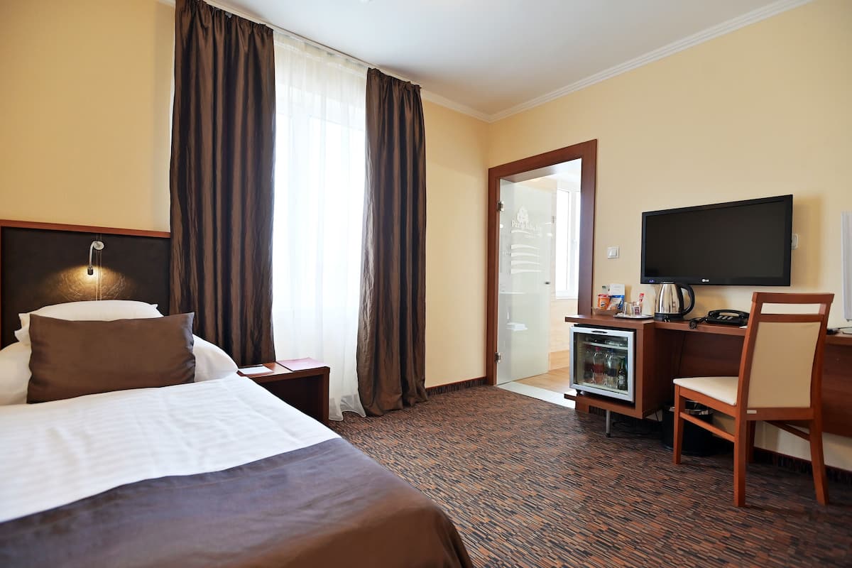 A hotel room with a bed, a desk, a television, and a minibar.