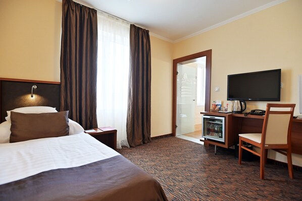 A hotel room with a bed, a desk, a television, and a minibar. - Hotel Eger & Park (Eger)